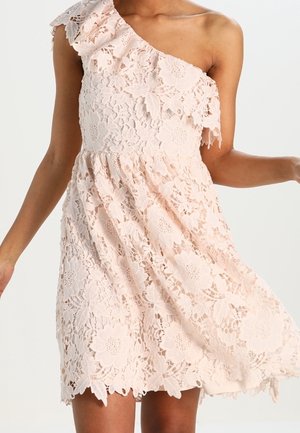 One-shoulder pale pink lace dress with floral pattern, fitted waist, and scalloped hem worn by a person.