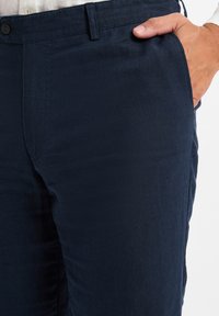 Dunkelblaue Leinenmischungshosen mit glatter Textur, ausgestattet mit einem Knopfverschluss und seitlichen Taschen, taillierte Passform und sauberer Verarbeitung.