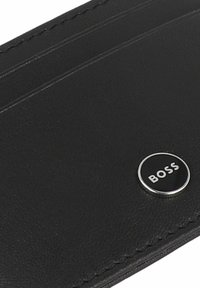 Portefeuille en cuir noir avec plusieurs emplacements pour cartes, finition texturée subtile et accent logo circulaire avec le mot "BOSS."