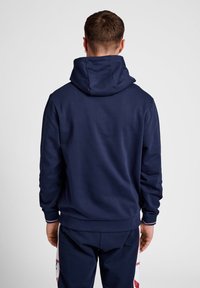 Marineblauwe hoodie met een grote, gestructureerde capuchon; zachte textuur; ribgebreide manchetten en zoom; minimalistisch ontwerp zonder zichtbare logo's of patronen.