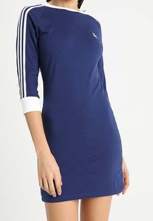 Marineblauwe getailleerde jurk met driekwart mouwen met witte strepen en een ronde halslijn, voorzien van een klein wit logo op de borst.