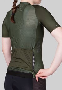 Camiseta deportiva de manga corta en verde oscuro, con textura de panal, bolsillo con cremallera lateral y acentos de goma en las mangas.