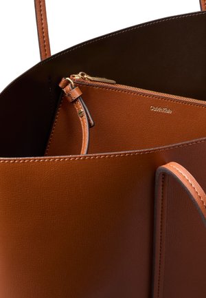 Braune Leder-Tasche mit passender Reißverschlusstasche innen, mit goldenem Reißverschluss und Calvin Klein-Logo auf der Tasche.