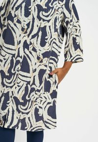 Navy and cream patterned coat with button closure, three-quarter sleeves, and side pockets. Textured fabric with abstract swirls.