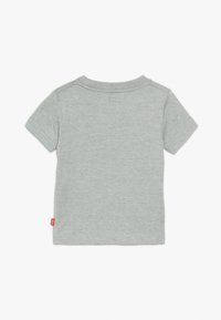 Camiseta de algodón gris de manga corta con cuello redondo, diseño sencillo y etiqueta de marca roja en el lateral. Textura suave, sin patrones.