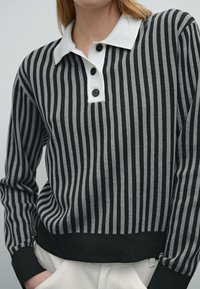 Long-sleeve, collared pullover in black and gray stripes. Features a white collar and three black buttons on the placket. Soft texture.