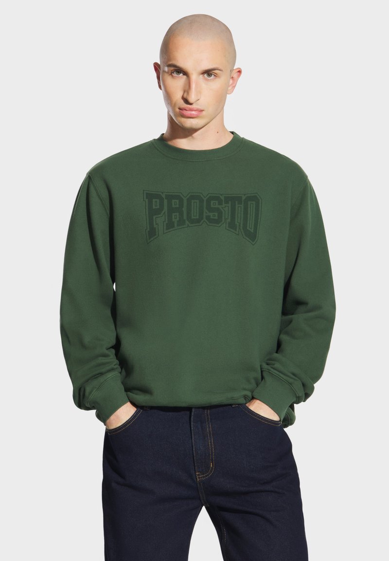 Zielona bluza z okrągłym dekoltem i dużym, ciemnozielonym nadrukiem "PROSTO" na klatce piersiowej. Posiada długie rękawy i ściągacze na mankietach.