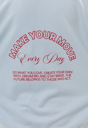 Texte rouge en gras sur tissu blanc : « FAITES VOTRE MOUVEMENT Chaque jour » et un message motivant sur l'amour, le courage et l'action en dessous.