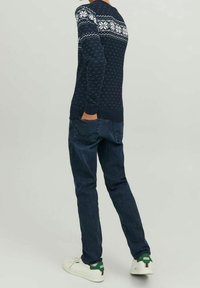 Námořnický pletený svetr s bílým sněhovým vzorem přes ramena, doplněný tmavě modrými džíny a bílými teniskami se zelenými akcenty.