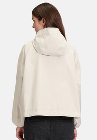 Lekka, kremowa kurtka z kapturem, o luźnym kroju i elastycznych mankietach. Gładka faktura, prosty design bez widocznych elementów metalowych.