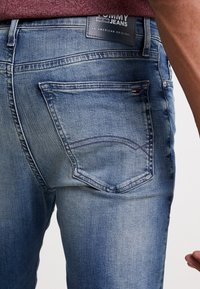 Blaue Denim-Jeans mit einem ausgewaschenen Look, ausgestattet mit einer Gesäßtasche mit geschwungener Naht und einem Markenetikett am Bund.
