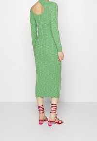 Abito verde a maglia con maniche lunghe, lunghezza a metà polpaccio, con dettaglio sulla schiena scoperta. Indossato con sandali rosa con cinturini.