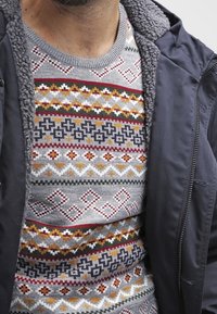 Maglione grigio a maglia con un motivo geometrico multicolore in rosso, giallo, verde e nero. Collo rotondo e superficie texturizzata.