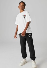 Hvid kortærmet t-shirt med blomsterprint, parret med sorte sweatpants med hvid logo-print. Skoene er hvide sneakers.