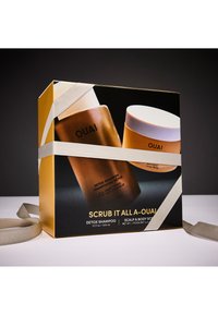 Gouden geschenkdoos met OUAI-producten: een bruine shampoo fles en een gouden pot met wit deksel. Tekst bevat "Scrub It All A-OUAI" en productdetails.