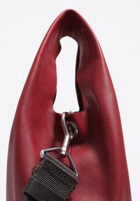 Raudona odinė rankinė su lygiu paviršiumi, turinti išpjautą rankeną ir sidabrinį užsegimą, pritvirtintą prie rudo diržo.