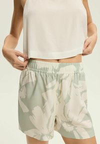 Szorty w kwiatowy wzór w delikatnym zielonym i kremowym kolorze, z elastycznym pasem. Połączone z lekką, bezrękawnikową białą bluzką.