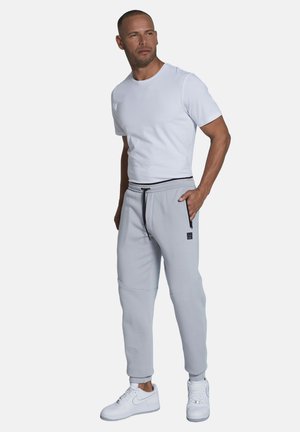 Light gray sweatpants with a drawstring waist, zippered pockets, and ribbed cuffs, paired with a fitted white T-shirt and white sneakers.