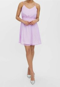 Ljuslila ärmlös klänning med v-ringning och rynkad midja. Transparent tyg med vita prickar. Kombinerad med silvriga högklackade skor.