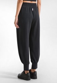 Svarta joggingsbyxor med avslappnad passform, elastisk midja, mudd vid anklarna och mjukt material, matchade med svarta sneakers.