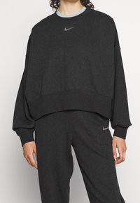 Czarna, ciemnoszara, skrócona bluza z kapturem z jasnoniebieskim kołnierzykiem, z małym, odblaskowym logo Nike na klatce piersiowej i luźnymi rękawami.