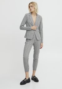 Svartvit rutigt kostym gjord av skräddarsytt tyg, med en figurnära kavaj med snibbkrage och smala byxor; matchat med svarta loafers.