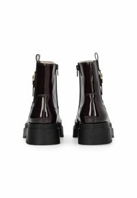 Botas de tobillo de charol burdeos con una plataforma negra gruesa, cierre de cremallera y herrajes dorados en el tacón, con un acabado suave y brillante.