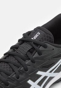 Black athletic shoe featuring a mesh upper, textured accents, flat laces, and a white logo along the side. Lightweight design for performance.