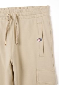 Beige sweatpants gemaakt van zacht materiaal, met een elastische tailleband, verstelbare trekkoord en cargozakdetail met logo-label.