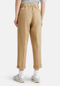 Beige, vysoké kalhoty s elastickým pasem, zúženými nohavicemi, ohrnutými manžetami a dvěma zadními kapsami. Texturovaná bavlněná tkanina.