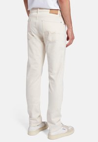 Jeans di colore crema con una vestibilità slim, dotati di tasche posteriori, dettagli di cucitura discreti e un'etichetta in pelle beige alla vita.