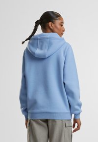 Modrá mikina s kapucňou vyrobená z mäkkej tkaniny, s šnúrkou na kapucni, rebrovanými manžetami a voľným strihom. Zdá sa, že má hladký povrch.