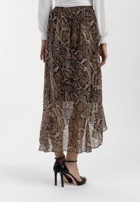 Gonna lunga a strati realizzata in materiale leggero e trasparente, con una stampa di serpente in tonalità marroni e beige. Abbinata a sandali neri con tacco alto.