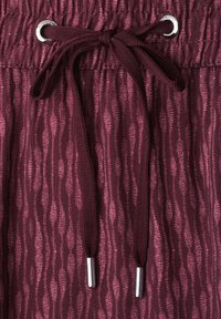 Close-up of burgundy patterned fabric with elastic waistband and tied drawstring featuring metal aglets and eyelets.