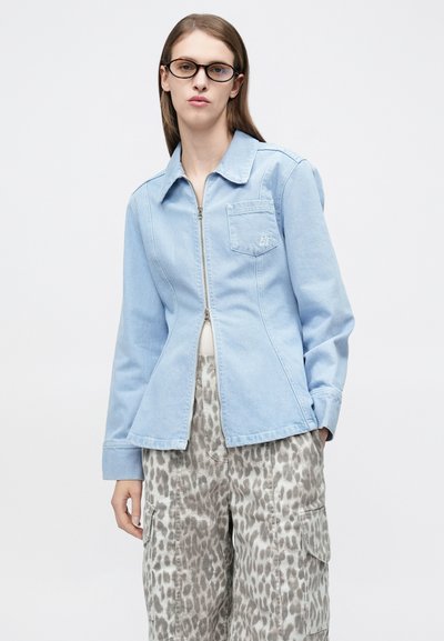 Ανοιχτομπλε τζιν μπουφάν με φερμουάρ, μυτερό γιακά και πλαϊνές τσέπες. Συνδυασμένο με γκρι παντελόνι cargo με ζωγραφιστό ζωικό μοτίβο.