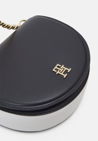 Rund handväska med marinblått läder på utsidan, vit botten och guldfärgade detaljer. Har en monogramlogotyp på framsidan och en kedjerem.