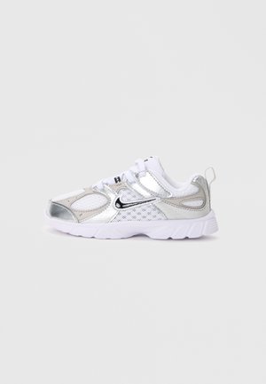Baskets Nike blanches et argentées avec panneaux en mesh, logo swoosh noir, lacets blancs et semelle blanche épaisse sur un fond gris clair uni.