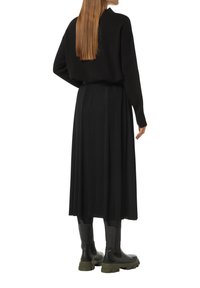 Black knit sweater paired with a pleated black skirt, and chunky black boots with a green sole, viewed from the back.