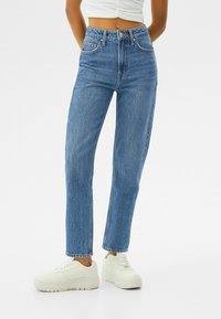Höga blå denimjeans med rak benpassform, försedda med framfickor, bälteöglor och en ljus tvätt. Matchas med vita sneakers.