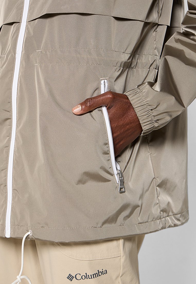 Giacca leggera beige con polsini elasticizzati, tasca con zip e zip bianca a contrasto. Materiale liscio e resistente all'acqua con una vestibilità comoda.
