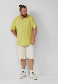 Luźna, krótko rękawowa żółta koszulka polo, zestawiona z jasnobeżowymi szortami do kolan i białymi sneakersami z beżowymi akcentami.