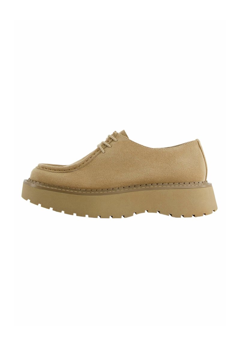 Zapatos derby de ante beige con punta redondeada, diseño de cordones y suela de goma gruesa con un patrón de textura en la banda de rodadura.