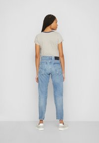 Camiseta de rayas gris con mangas cortas y ribete azul marino, combinada con pantalones vaqueros de cintura alta en azul claro y zapatillas blancas. Vista trasera.