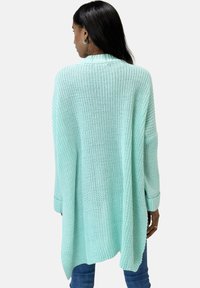 Mintgrüner, übergroßer Strickcardigan mit einem strukturierten Muster, mit herunterhängenden Schultern und gerippten Bündchen, getragen über Denim-Jeans.