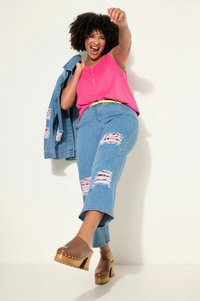 Rosa ärmlös topp, ljusblå slitna denimjeans med rosa detaljer, och bruna träklackar. Denimjacka hängande över armen.