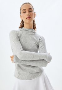 Lysegrå langærmet bluse med mock neck, struktureret mønster og tommelhuller. Båret med en hvid nederdel.