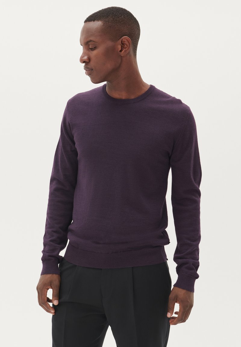 Ljubičasti pulover s okruglim izrezom i dugim rukavima, s rebrastim manžetama i donjim rubom, izrađen od mekanog materijala, uparen s crnim hlačama.