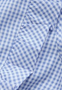 Blauw-witte gingham stof met een gestructureerde oppervlakte, met een gerimpelde rand aan één kant en een geruit patroon over het geheel.