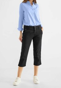 Černé zkrácené kalhoty s rovnými nohavicemi, dvěma předními kapsami a stříbrnými knoflíky, doplněné světle modrou dlouhým rukávem.