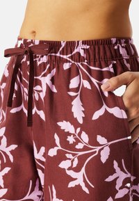 Bordeauxrode broek met een lichtroze bloemenpatroon, elastische tailleband met trekkoord, zijzak en zachte, gestructureerde stof.